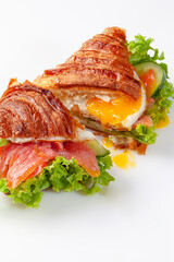 Croissant sandwich cut in half with fried egg, salted salmon, fresh lettuce and cucumber