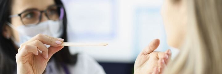 Female doctor examining throat of patient with wooden spatula closeup