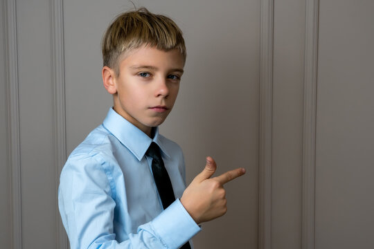 School boy in blue shirt with black tie looking to camera and pointing with hand and finger to the side
