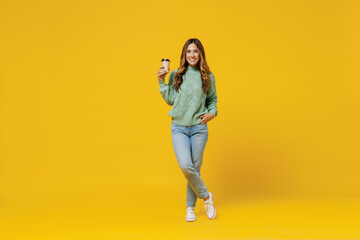 Fototapeta na wymiar Full body young smiling woman 30s in green knitted sweater hold takeaway delivery craft paper brown cup coffee to go isolated on plain yellow color background studio portrait People lifestyle concept