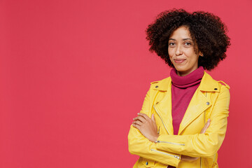 Obraz na płótnie Canvas Charming bright young curly black latin woman 20s years old wears yellow jacket looking camera hold hands crossed isolated on plain red background studio portrait. People emotions lifestyle concept.
