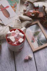 A mug with marshmallows, a white sweater, toys on a light photo background.