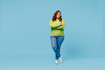 Full body confident happy young chubby overweight plus size big fat fit woman wear green sweater hold hands crossed folded isolated on plain blue background studio portrait. People lifestyle concept. - obrazy, fototapety, plakaty