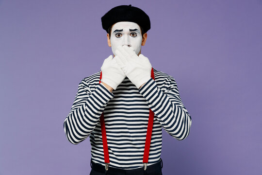 Secret embarrassed bewildered puzzled bemused sad young mime man with white face mask wears striped shirt beret cover mouth with hand isolated on plain pastel light violet background studio portrait.