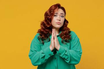 Pleading bright vivid young ginger chubby overweight woman 20s years old wears green shirt hands folded in prayer gesture begging about something isolated on plain yellow background studio portrait.