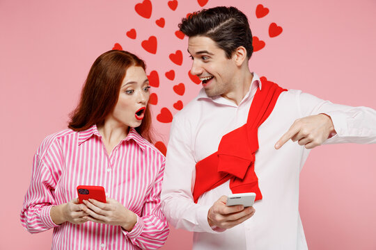 Young Couple Two Friends Woman Man 20s In Casual Shirt Using Point Finger On Mobile Cell Phone Isolated On Plain Pastel Pink Background Studio Portrait. Valentine's Day Birthday Holiday Party Concept