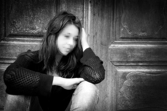 Black and white photo of a sad anonymous young woman with pixelated face who is thoughtful about troubles in front of a gray wall