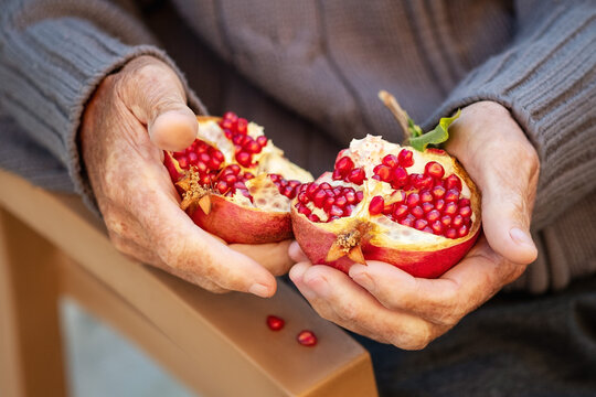 Ripe organic broken pomegranate, cut in half in senior hands .Selective focus,top view.