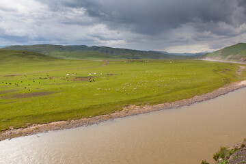 landscape with hills, grasslands and a river under overcast sky in the Qi Lian mountains, Qinghai province, China