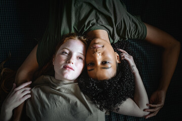 A couple of multiracial lesbian women lying down on the bed caressing each other - gay female homosexual concept