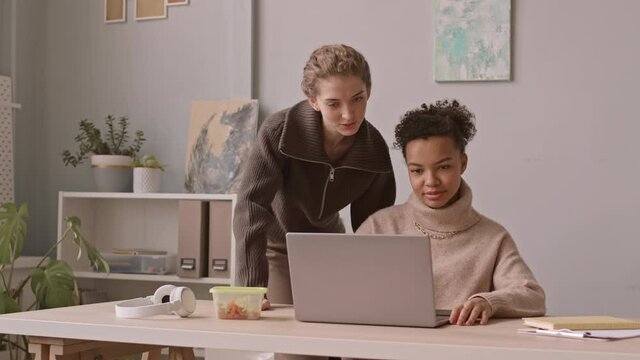 Medium slowmo shot of two female designers discussing collaborative project on laptop while working together in cozy office