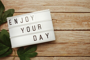 Enjoy Your Day text on lightbox on wooden background