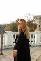 Fototapeta na wymiar A young beautiful woman in a black coat walks around the city