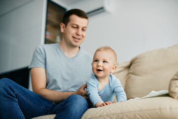 Obraz premium Happy baby boy crawls on sofa while spending time with his father at home.
