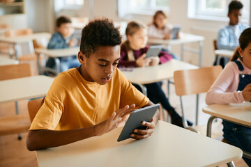 Black schoolboy e-learning on digital tablet during class in classroom.