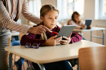 Little girl uses touchpad with teacher's assistance during class at elementary school.
