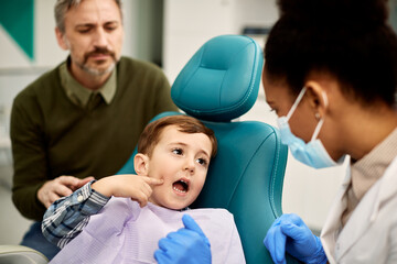 Small boy complains about toothache to his dentist during dental check-up.