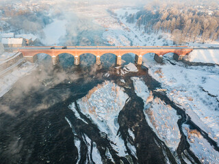 River Venta and long brick bridge in foggy winter day, Kuldiga, Latvia. Captured from above