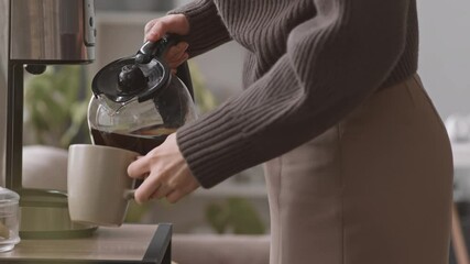 Midsection slowmo shot of unrecognizable woman pouring coffee from drip coffee maker in office