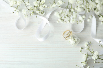 Concept of wedding accessories with wedding rings on white wooden background
