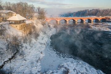 River Venta and long brick bridge in foggy winter day, Kuldiga, Latvia. Captured from above