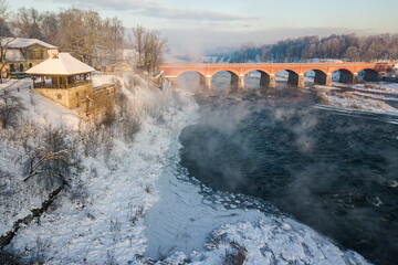 River Venta and long brick bridge in foggy winter day, Kuldiga, Latvia. Captured from above