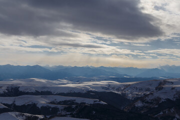 The setting sun illuminates the mountain range through the clouds