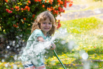 Child watering flowers and plants in garden. Kid with water hose in backyard. Kids gardening. Kids...