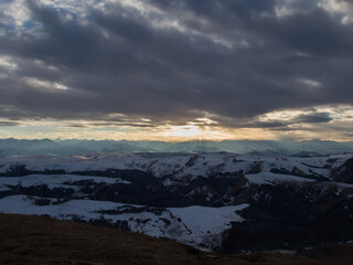 Fototapeta na wymiar The setting sun illuminates the mountain range through the clouds