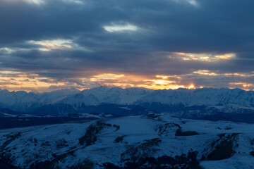 The setting sun illuminates the mountain range through the clouds