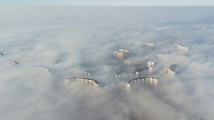 Silhouettes of tall houses through the incoming thick fog. Megalopolis in white clouds in the early morning at time.