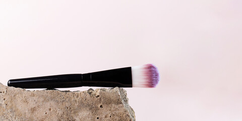 Cosmetic brush for blush, softening near a grey stone. Copy space.