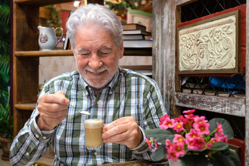 Portrait of smiling elderly bearded grandfather sitting holding a cup of coffee with milk putting a...