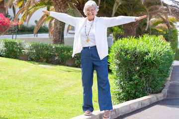 Playful mature woman walking  in balance with her arms outstretched. Attractive elderly woman looking at camera smiling
