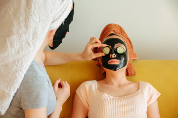 woman applies slices of cucumber on her friends eyes. cosmetic procedures, mask for skin care,