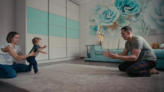 Happy family smiling as baby takes first steps. Family At Home Encouraging Baby Son To Take First Steps.