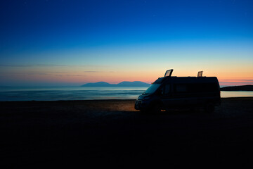  Silhouette of camper van, motorhome standing on abandoned beach against colorful sunset sky,  van...
