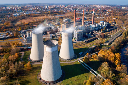 Aerial view of typical coal thermal power plant complex with cooling towers in operation and city in the background.