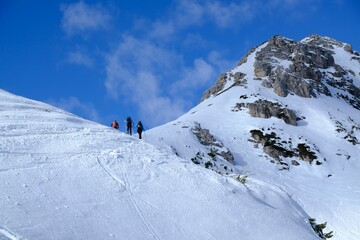 Silhouettes of skiers during backcountry skis through snowy mountains on a sunny day. Silhouettes of skiers on trail. During trip in Dolomites around Tre Cime. Sexten Dolomites, South Tyrol, Italy