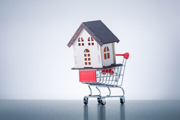 House model in shoppihg trolley on grey background with copy space. Real estate concept, buy house.