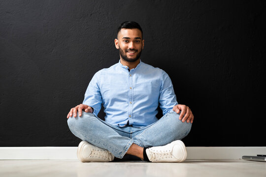 Man with cross-legged sitting by wall in studio