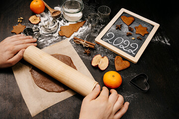 Baking Christmas gingerbread cookies on a dark wooden table. Preparing for baking. Winter holidays. 2022 New Year sign. Top view. 