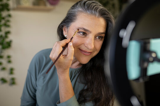 Smiling female vlogger brushing eyebrows during tutorial at home