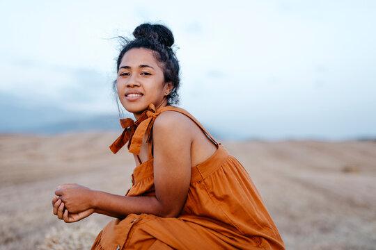 Smiling young woman sitting in farm during sunset