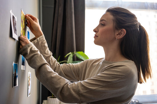 Young woman sticking photograph on wall at home