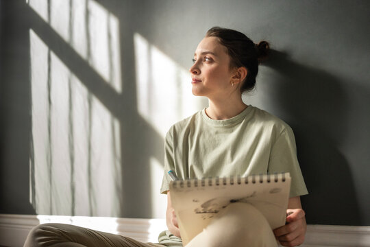 Thoughtful woman with note pad leaning on wall
