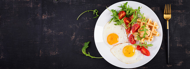 Breakfast with cheese waffles, fried eggs, tomato, hummus and arugula on dark table. Appetizers, snack, brunch. Healthy vegetarian food. Top view, banner