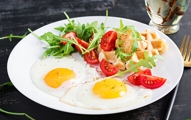 Breakfast with cheese waffles, fried eggs, tomato, hummus and arugula on dark table. Appetizers, snack, brunch. Healthy vegetarian food.