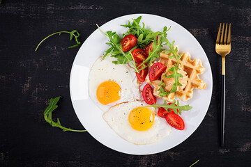 Breakfast with cheese waffles, fried eggs, tomato, hummus and arugula on dark table. Appetizers, snack, brunch. Healthy vegetarian food. Top view, overhead