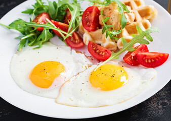 Breakfast with cheese waffles, fried eggs, tomato, hummus and arugula on dark table. Appetizers, snack, brunch. Healthy vegetarian food.